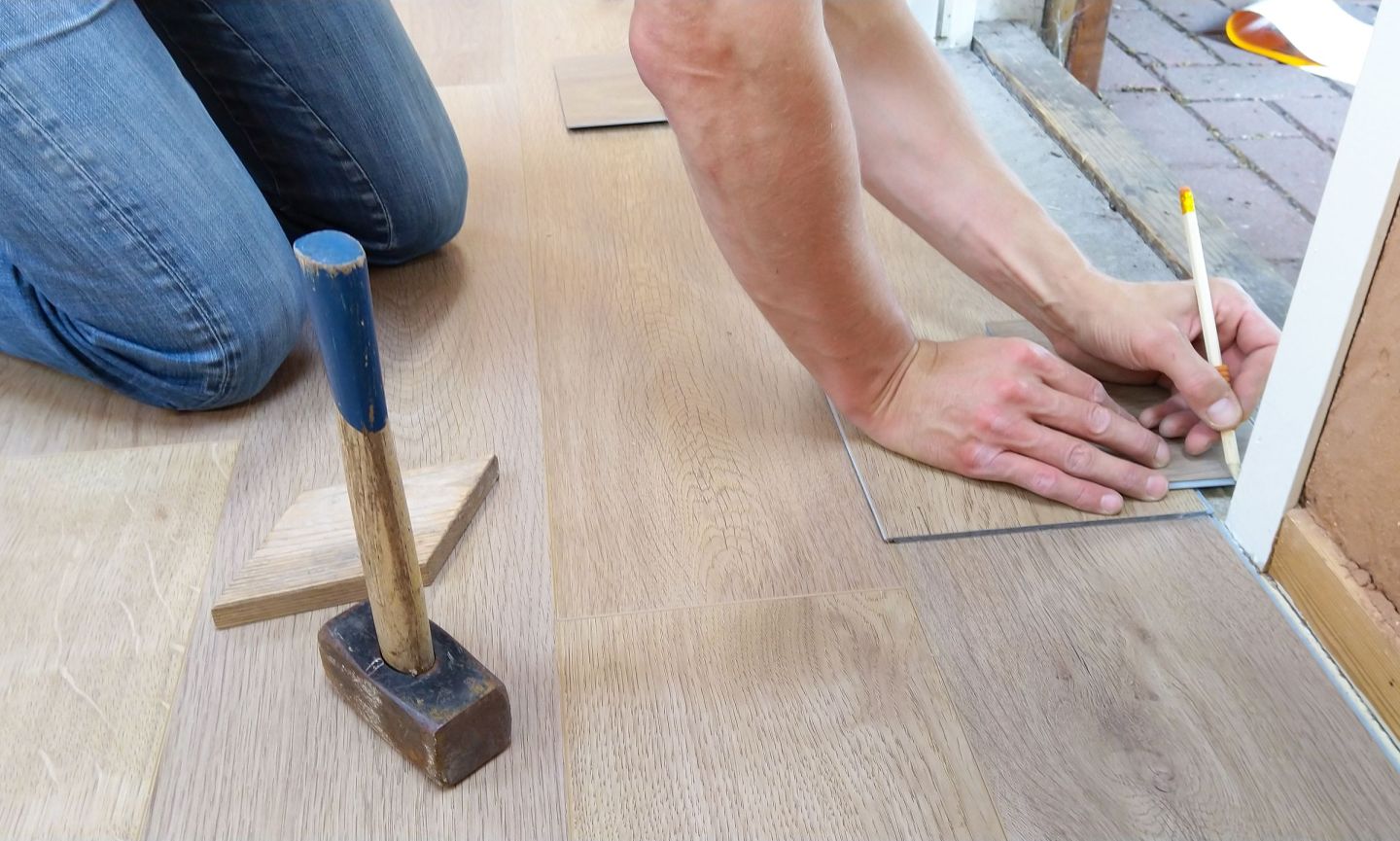 Handwerker misst eine Bodendiele ab und zeichnet die Schnittkante mit einem Stift an