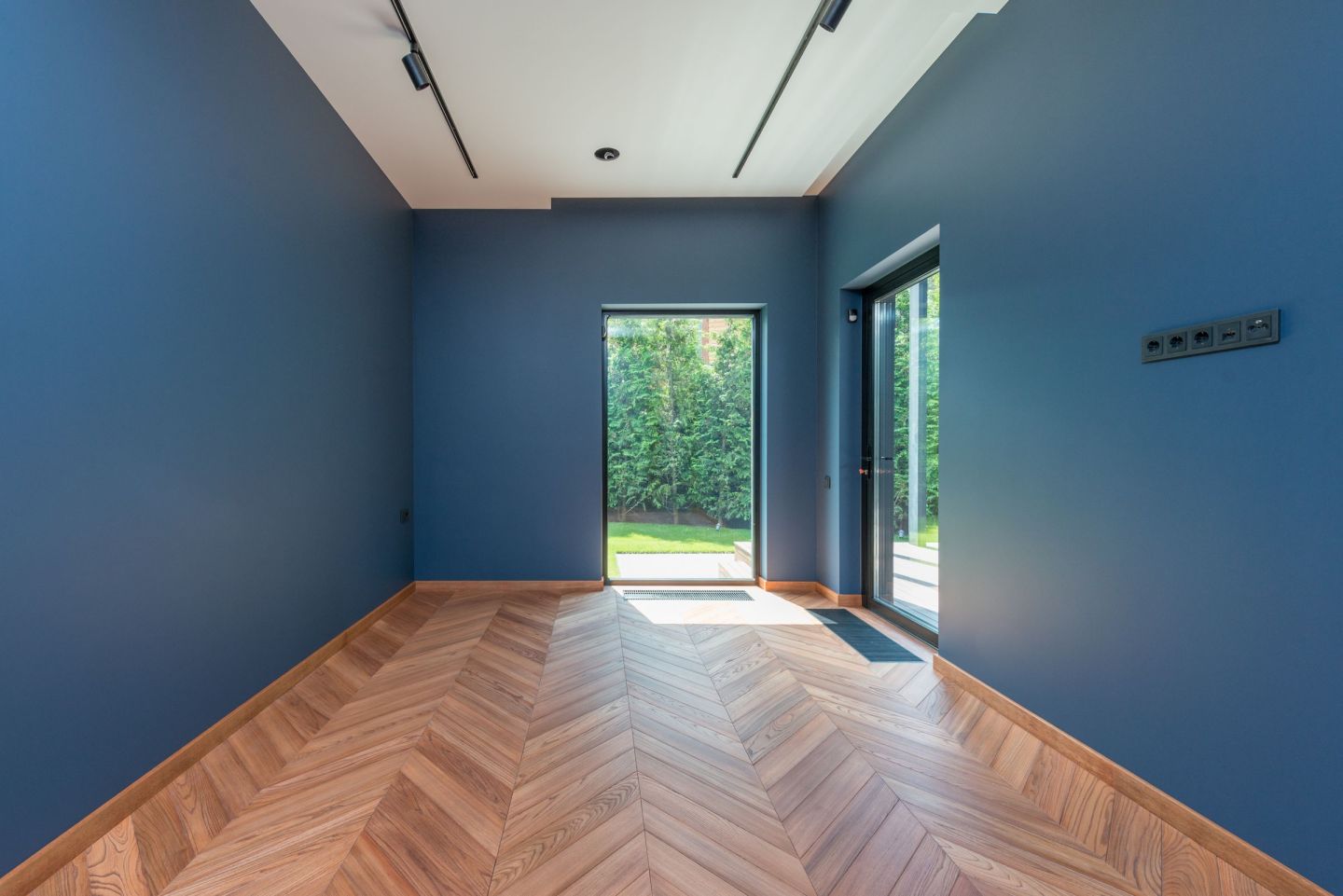 Wohnraum mit blauen Wänden und einem Holzboden im Fischgrätverband, Blick durch den Raum auf große Fenstertüren