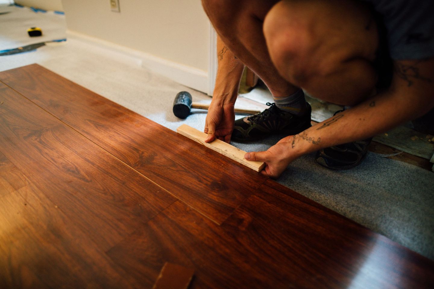 Handwerker schlägt eine Laminatdiele mit Schlagklotz und Hammer an die vorherige Reihe an